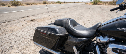 Harley Road Glide bagger parked at desert roadside pull-off, factory black vinyl seat baking in midday sun, long-ride fatigue