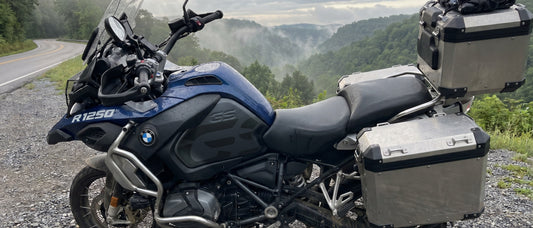 Motorcycle saddle cover buyer guide, BMW R1250 GS adventure tourer parked on tree-lined mountain switchback at dawn