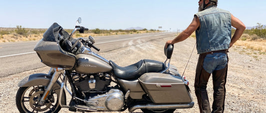 Rider standing beside parked Harley Road Glide at a roadside pull-off, stretching after a long motorcycle ride