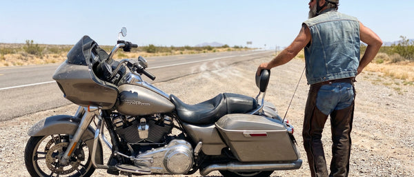 Rider standing beside parked Harley Road Glide at a roadside pull-off, stretching after a long motorcycle ride